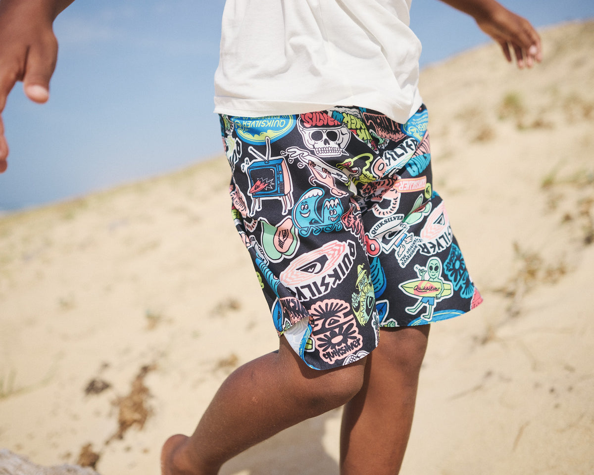 Person wearing colorful graphic shorts walking on a sandy beach.