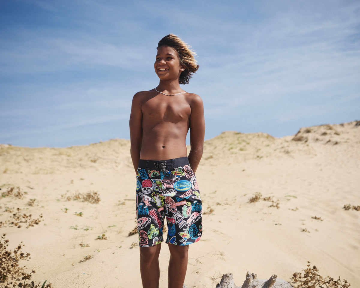 Person wearing colorful swim shorts standing on sand dunes with a clear blue sky.