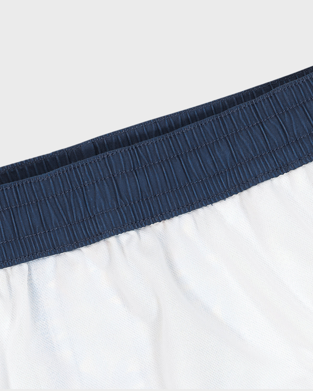 Close-up of white shorts with a navy waistband on a light gray background