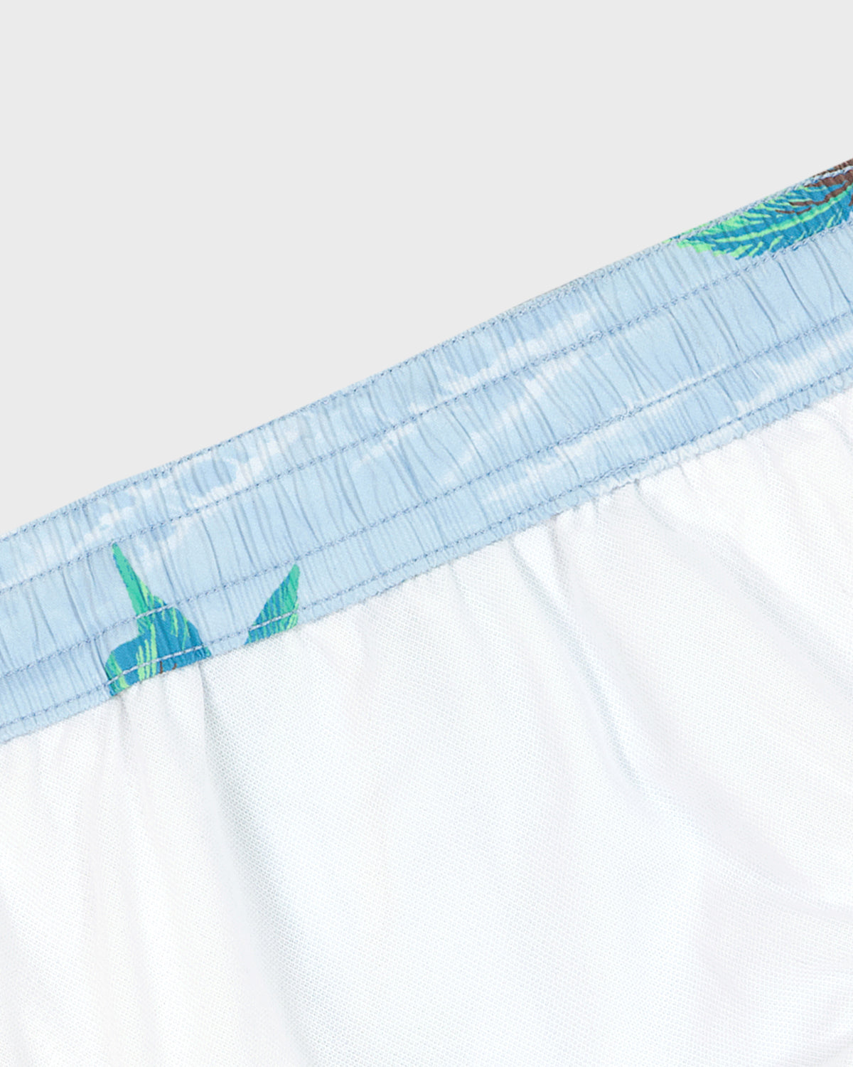Close-up of white boxer briefs with blue and green trim on a light gray background